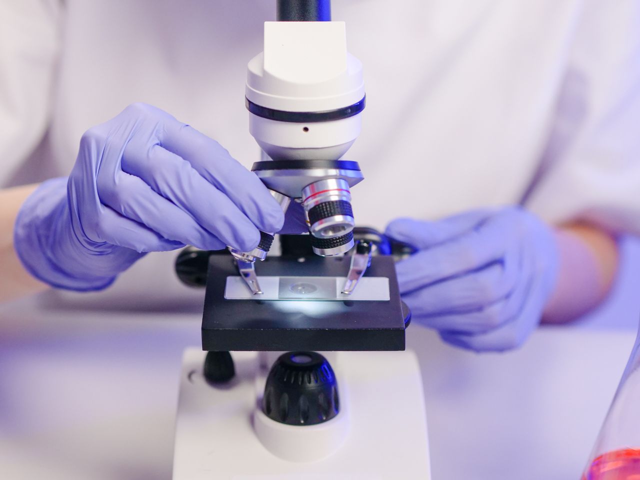Scientist wearing gloves using a microscope in a laboratory setting.