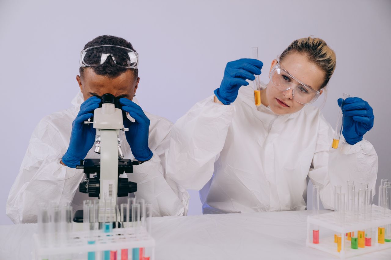 Two scientists in lab coats conduct research with a microscope and test tubes in a laboratory.